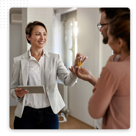 A smiling real estate agent hands keys to a couple inside a bright, modern home, while holding a tablet and using an automation tool to streamline sales.