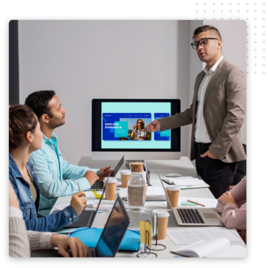 A man in a suit presents sales marketing funnel strategies to three colleagues in a modern office. They review a website on the screen, surrounded by laptops, notebooks, and coffee cups.
