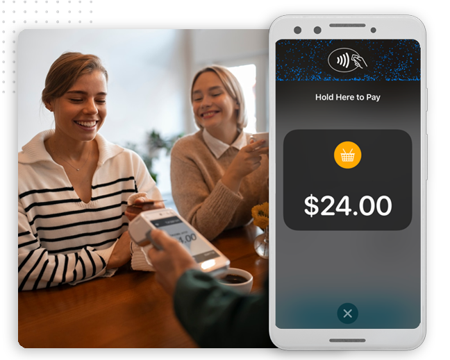 Two women smile at a table as one pays with her smartphone using contactless payment; a mobile screen in the foreground displays a $24.00 purchase—effortless transactions powered by automation company innovations.
